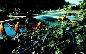 Workers in lime coats standing on rugged coastline utilizing liquid hoses to clean within the oil spill from the Exxon Valdez. (Due To Richard Stapleton. Reproduced by authorization.)